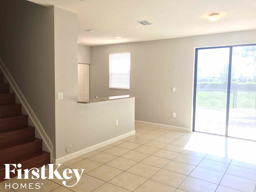 A spacious room with a staircase on the left and a sliding glass door on the right.