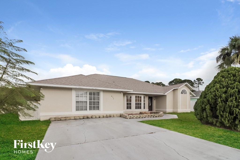 a beige house with a driveway and a palm tree