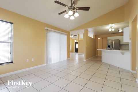 an empty living room with a ceiling fan and a kitchen