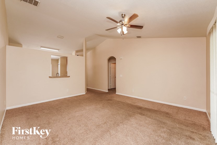 a spacious living room with carpet and a ceiling fan