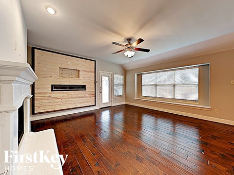 an empty living room with wood floors and a large window and a ceiling fan
