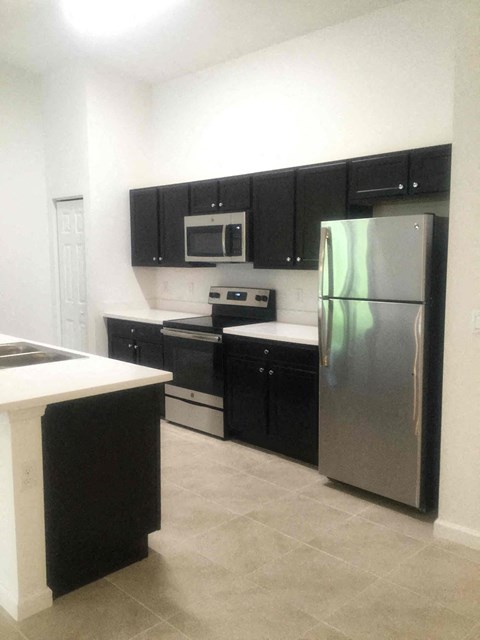 A kitchen with black cabinets and a stainless steel refrigerator.