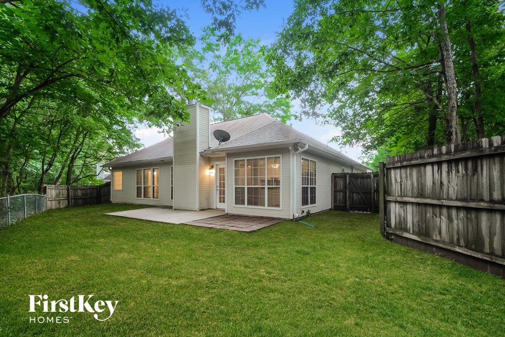 a backyard with a white house and a green lawn and a fence