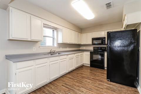 A kitchen with white cabinets and a black fridge.