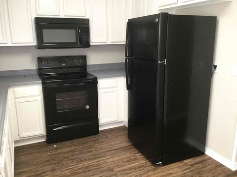 A black refrigerator stands in a kitchen next to a black oven.