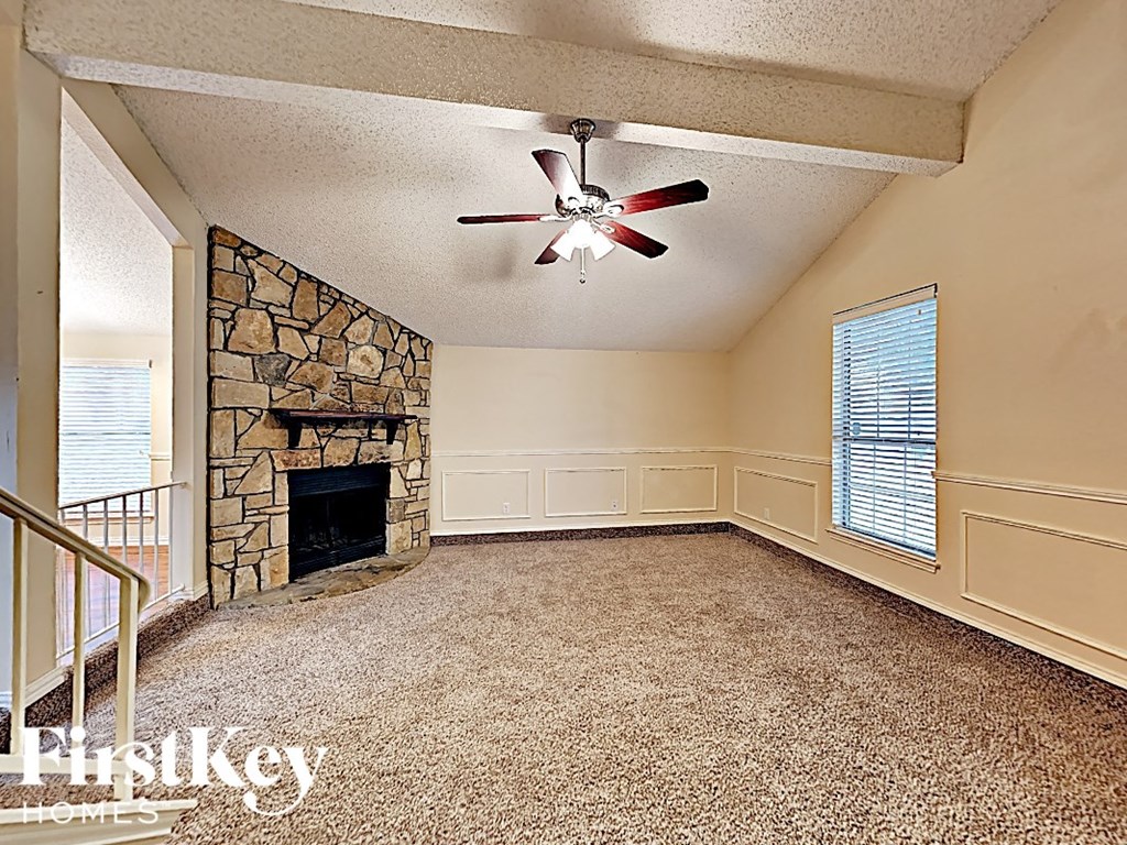 A room with a stone fireplace and a ceiling fan.