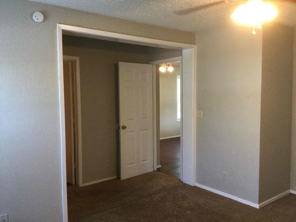 an empty living room with a white door and a hallway to a bedroom
