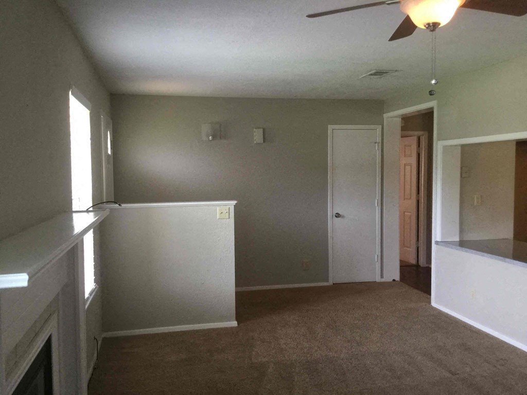an empty living room with a kitchen and a door to a hallway