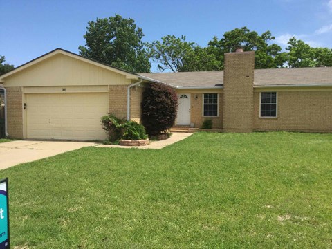 a tan brick house with a lawn and a driveway