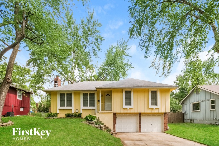 A yellow house with a red house and a tree in the background.