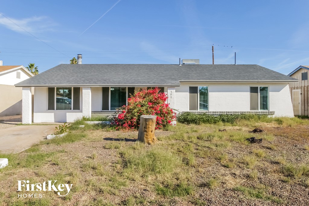the front of a white house with a tree stump in the yard
