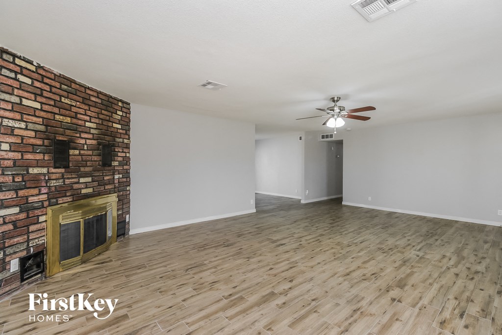 a living room with a brick fireplace and wooden floors and a ceiling fan