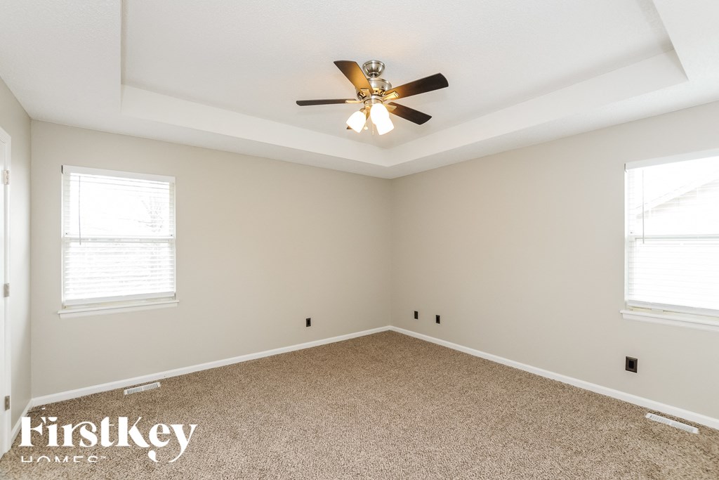 A room with a ceiling fan and two windows.