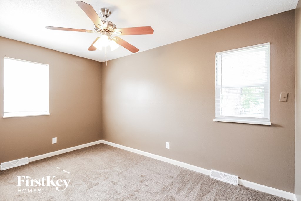 an empty room with a ceiling fan and two windows