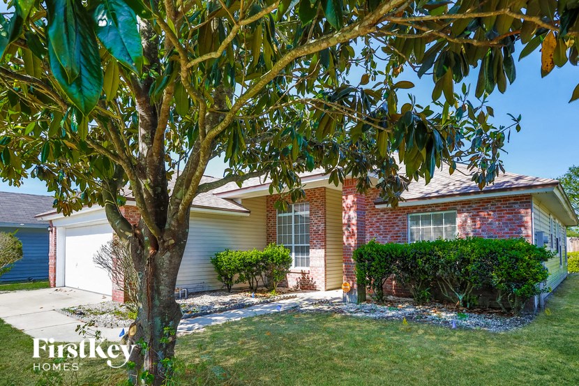 A tree in front of a brick house with a sign that says "Firstkey Homes".