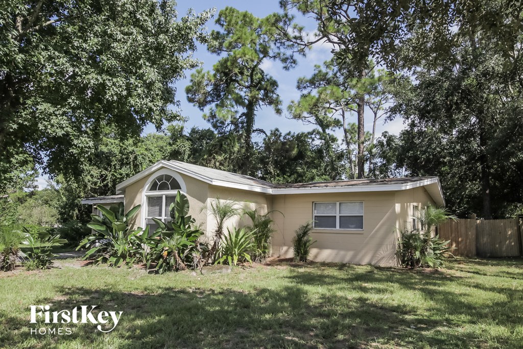 a small tan house with a lawn and trees