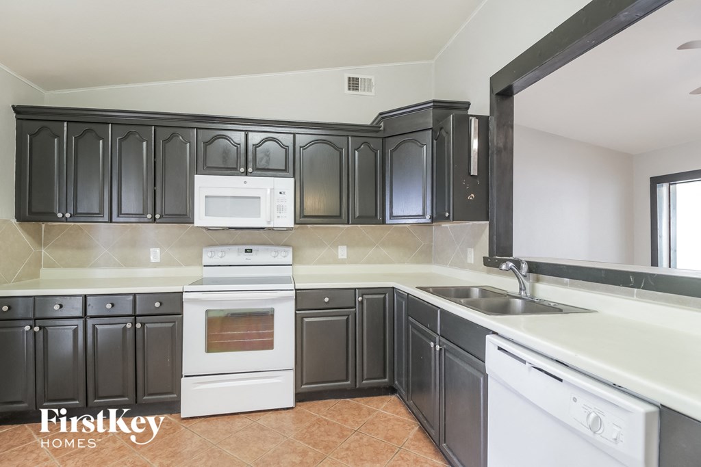 an empty kitchen with black cabinets and white appliances