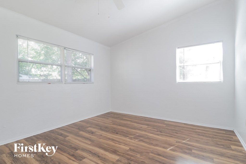 a bedroom with white walls and wood flooring and two windows
