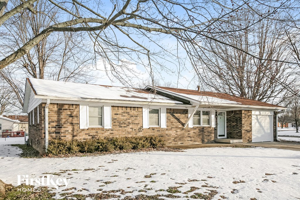 A house with a snow-covered ground and bare trees in the background.
