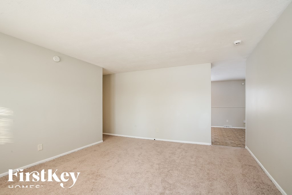 A spacious room with a carpeted floor and white walls, with a FirstKey Homes logo in the bottom left corner.