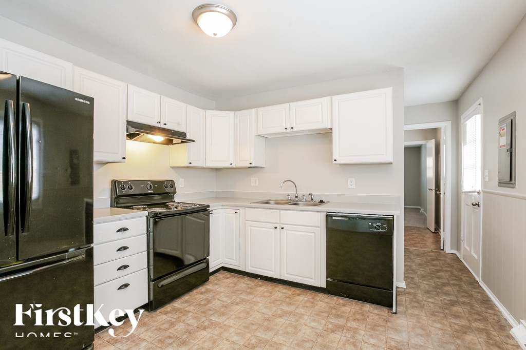 A kitchen with white cabinets and a black fridge.