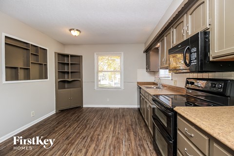 A kitchen with wooden floors and a black microwave above the stove.
