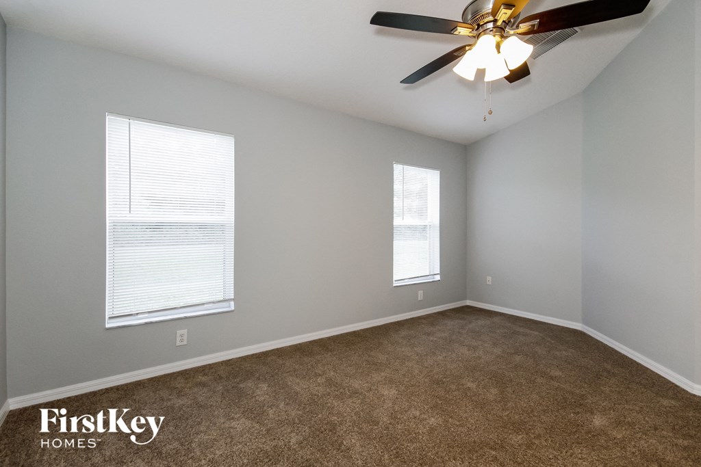 an empty living room with a ceiling fan and two windows