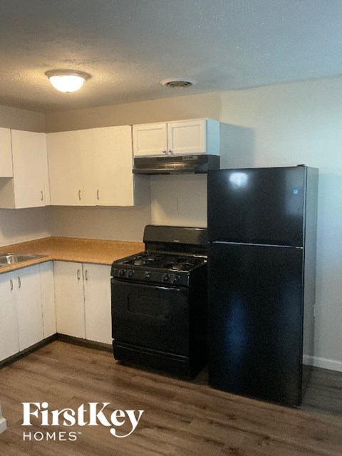 A black fridge and stove in a kitchen with white cabinets.