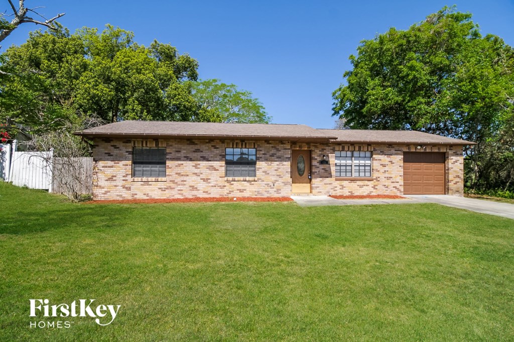 A house with a brown roof and a brown garage door is surrounded by a green lawn.