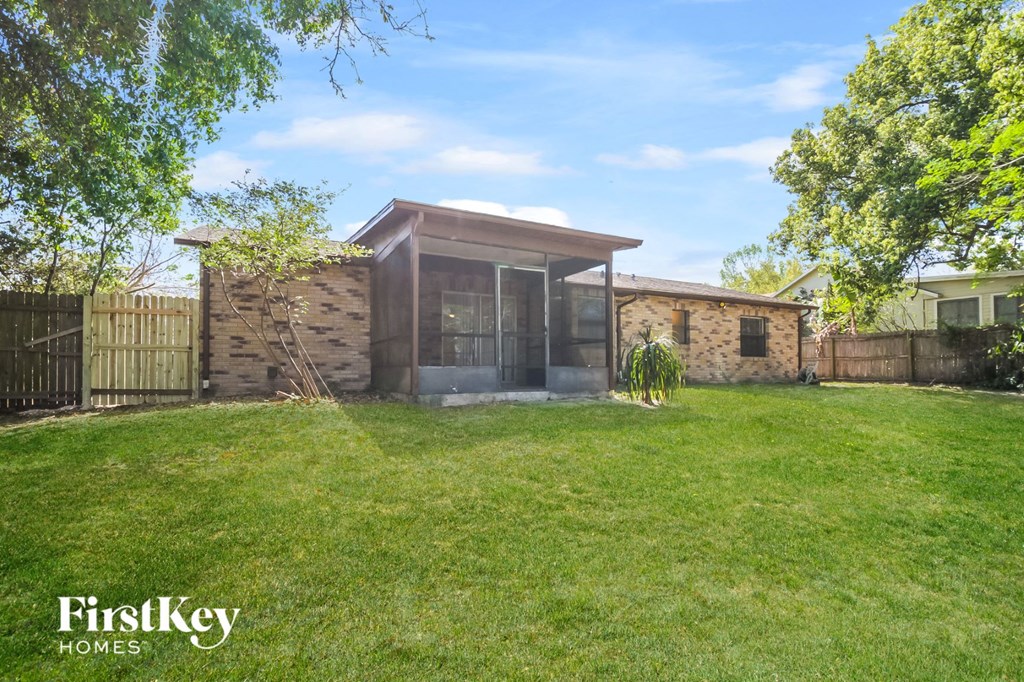 A house with a brown roof and a glass door is surrounded by a fence and green grass.