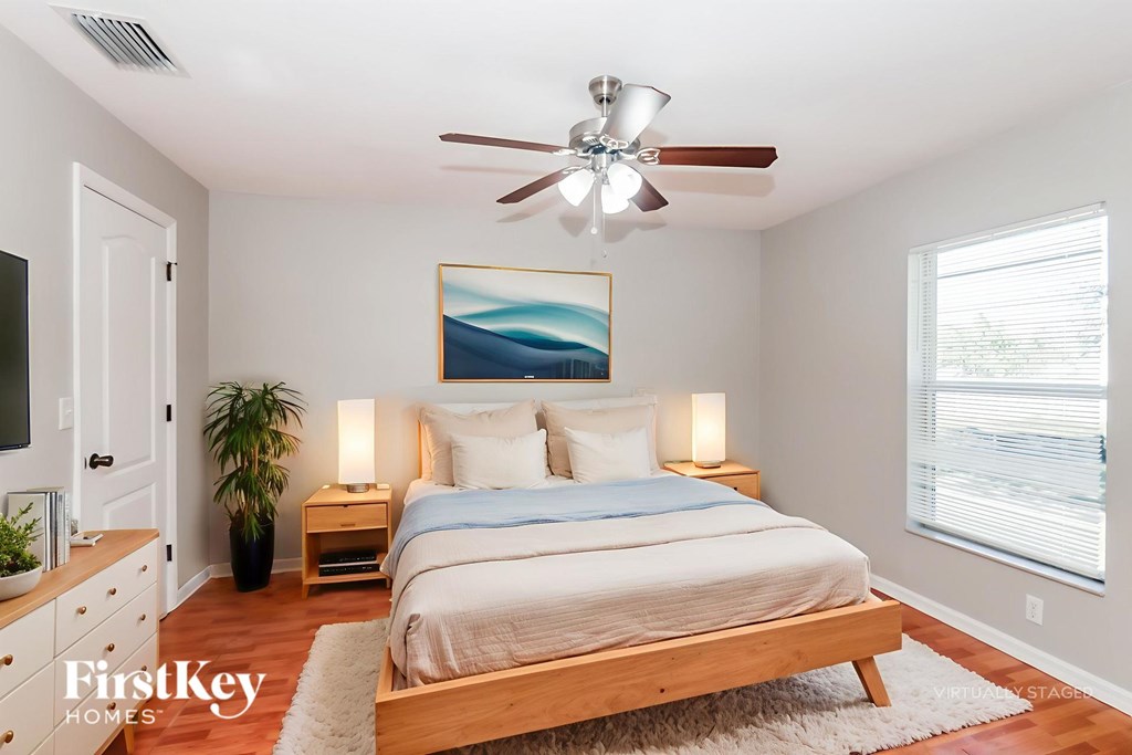 A bedroom with a bed, a ceiling fan, and a painting on the wall.