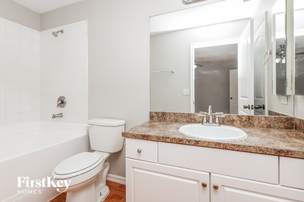 A white bathroom with a marble counter top and a white toilet.