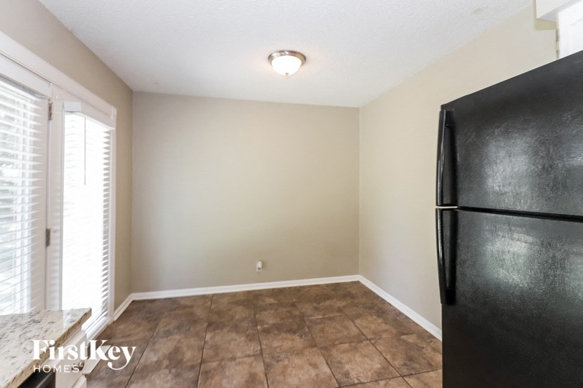 A black fridge sits in a room with a tile floor and a window with blinds.