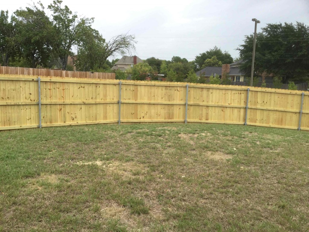 a wooden fence in a backyard with a grass field