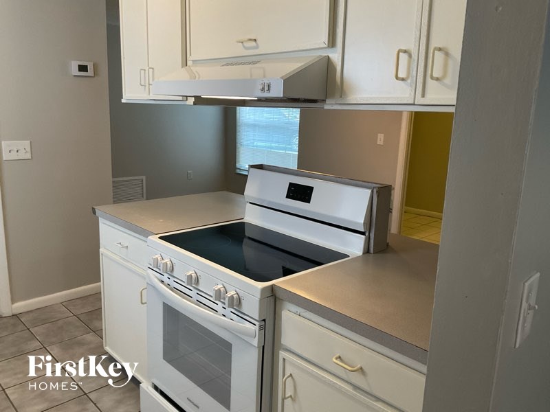A white stove top oven with a black glass top is in a kitchen.
