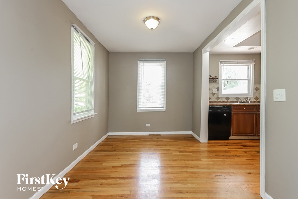 an empty dining room and kitchen with wood floors and two windows