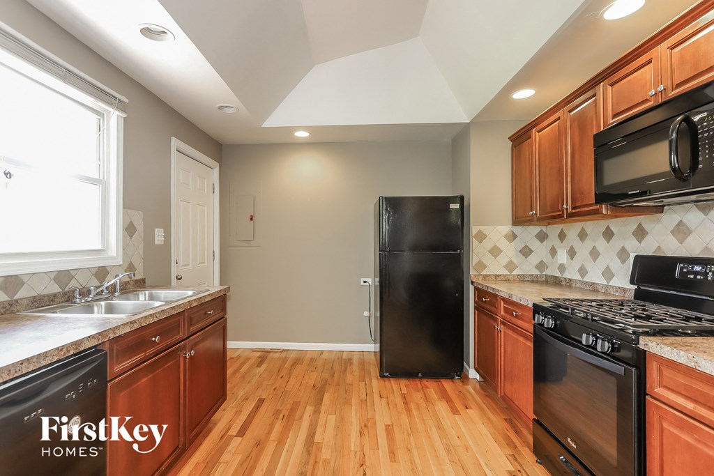a kitchen with wooden cabinets and black appliances and a wood floor