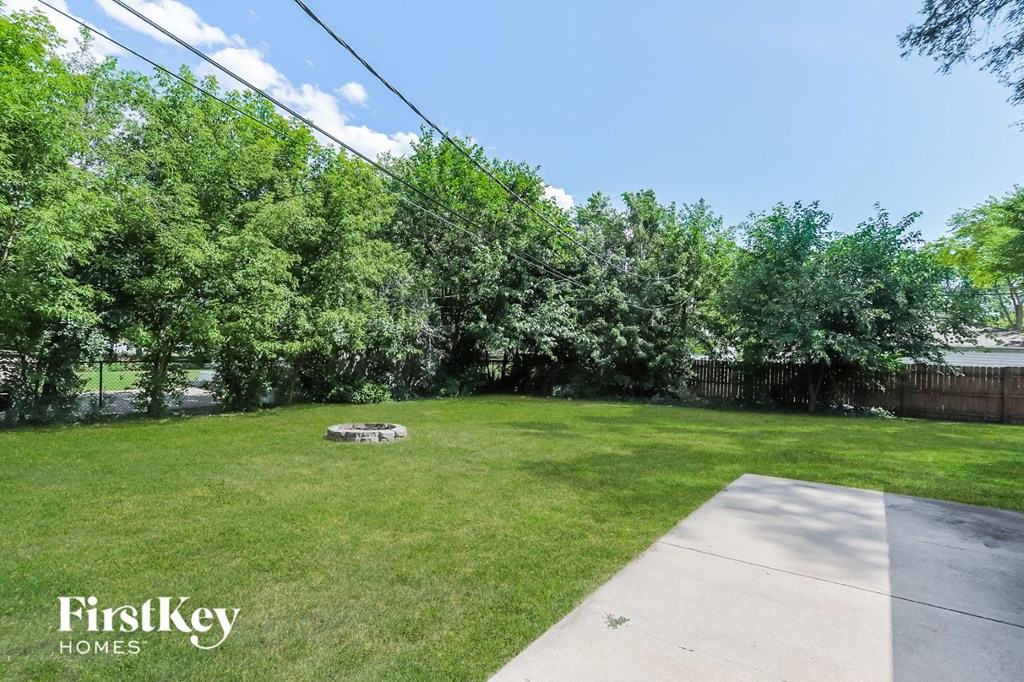 a backyard with green grass and trees and a fire pit