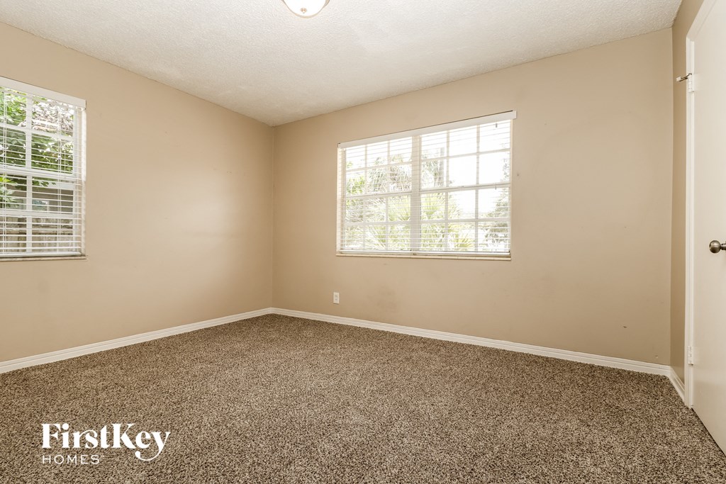 A room with a carpeted floor, a window with blinds, and a door.