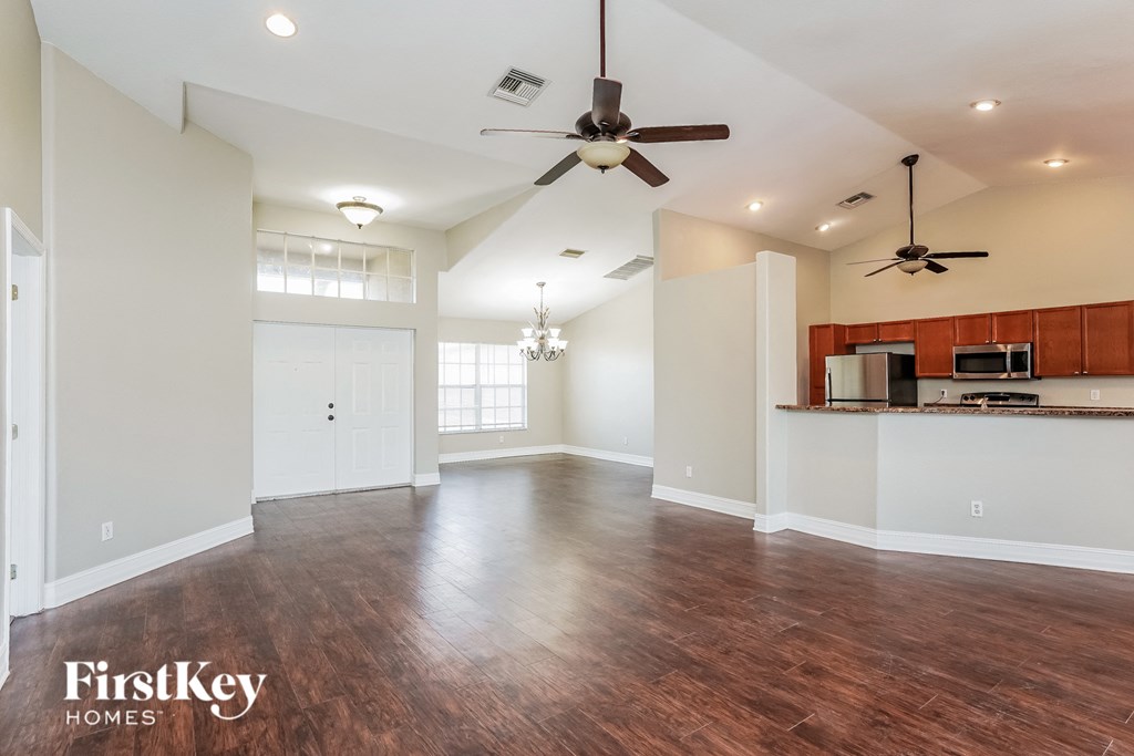 an empty living room with a ceiling fan and a kitchen