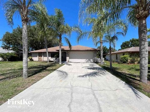 A house with a driveway and palm trees in front.