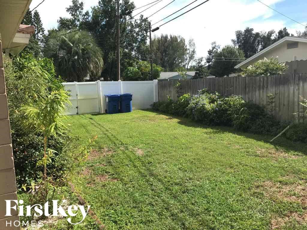 a backyard with grass and a fence and a blue trash bin