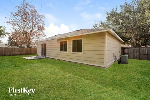 a small tan building in a backyard with a lawn and a fence