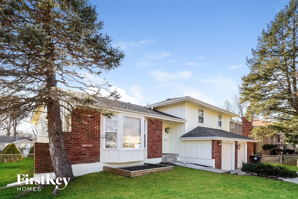 a small white and brick house with a yard and a tree
