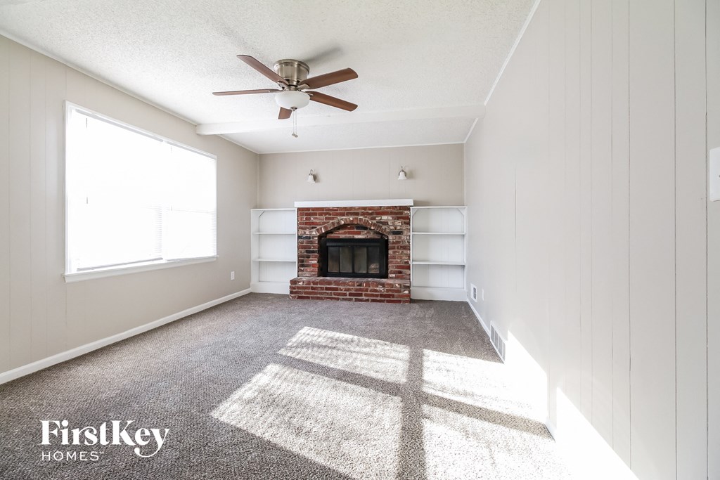an empty living room with a brick fireplace and a ceiling fan