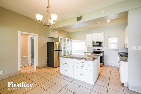 A kitchen with white cabinets and appliances, a black refrigerator, and a chandelier hanging from the ceiling.