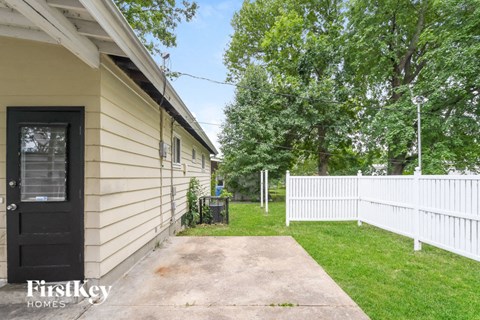 the side of a house with a sidewalk and a white fence