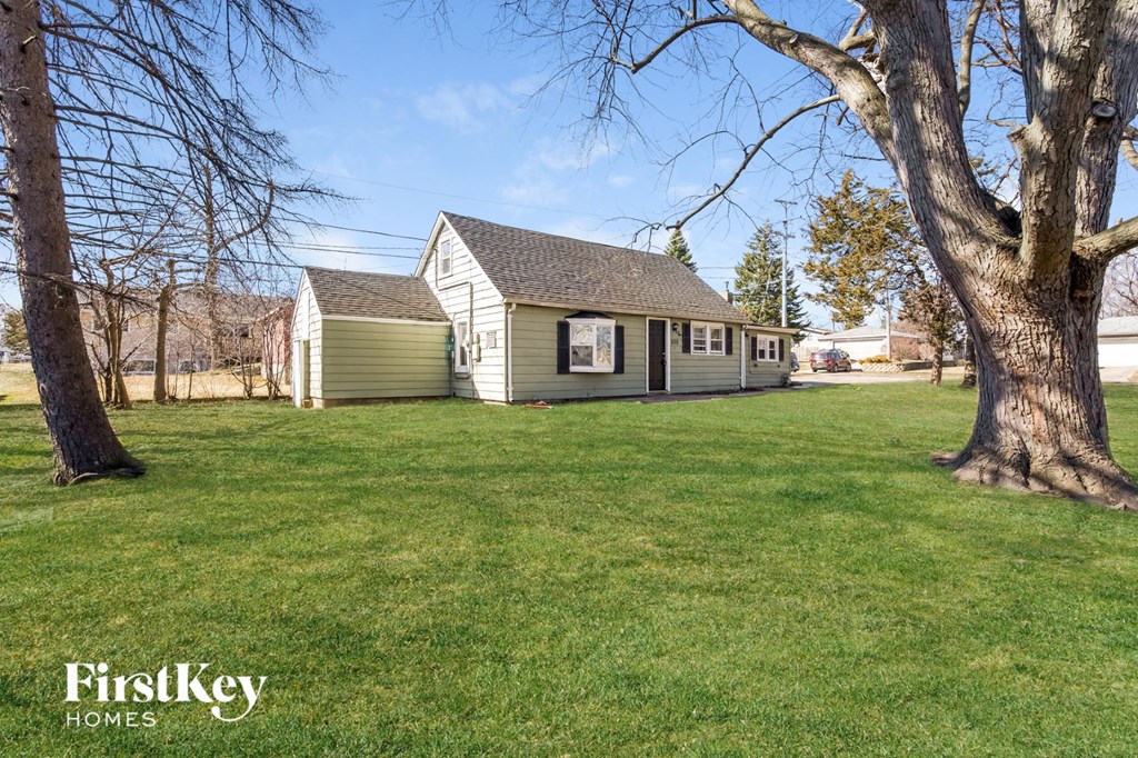 a small white and green house with a yard and two trees