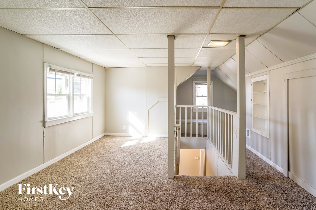 a bonus room with a staircase and white walls and carpet