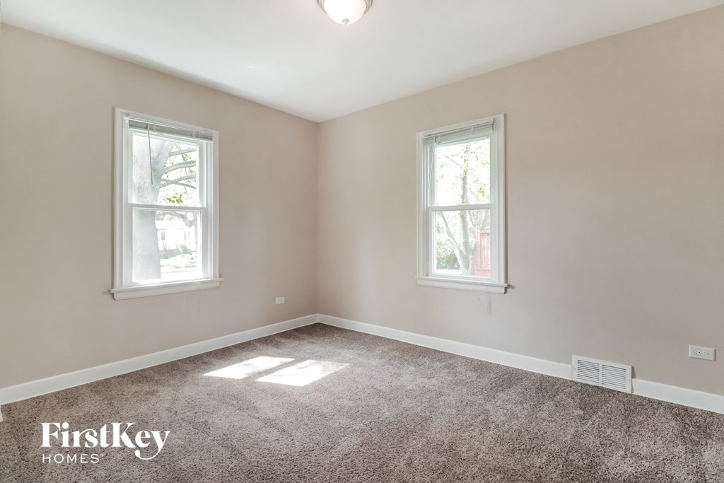 an empty bedroom with two windows and a carpeted floor